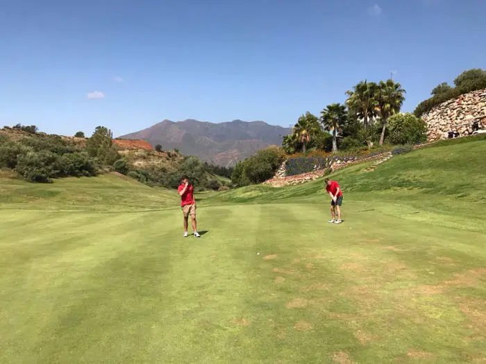 Golfers putting out on the green with mountains in the background