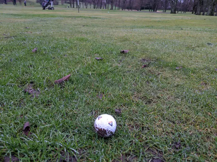 A golf ball in the fairway with mud on
